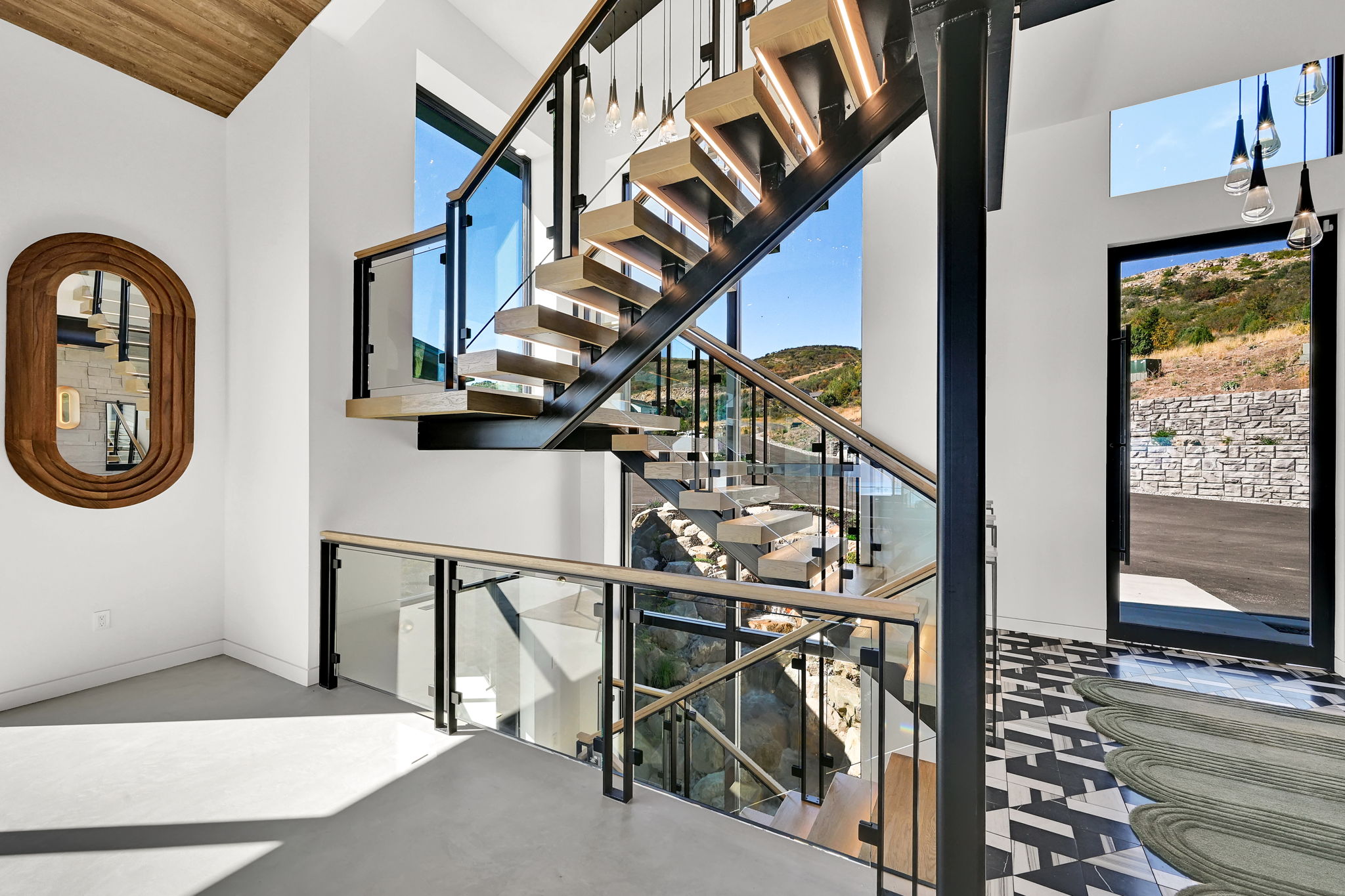 A floating oak and steel staircase with glass railings and pendant lights